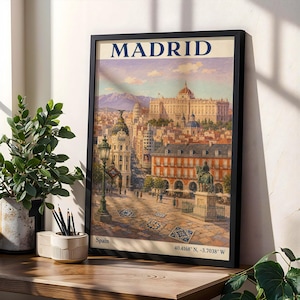 May include: A framed wall art print featuring a vintage-style illustration of Madrid, Spain. The image depicts a city square with a statue, a street lamp, and the Royal Palace in the background. The text reads MADRID, Spain, and 40.4168 N, -3.7038 W.