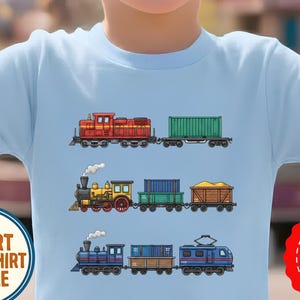 以下が含まれることがあります： 3種類の列車が描かれたライトブルーのTシャツ。一番上の列車は赤色で緑色のコンテナを牽引しています。真ん中の列車は黄色と黒色で2両の貨車を連結しています。一番下の列車は青色で2両の貨車を連結しています。