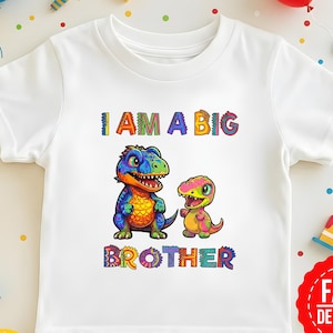 Może przedstawiać: Biała koszulka z kolorową grafiką przedstawiającą dwa dinozaury i napisem "I AM A BIG BROTHER". Dinozaury są w odcieniach niebieskiego, zielonego, pomarańczowego i żółtego. Tekst jest wielokolorowy.
