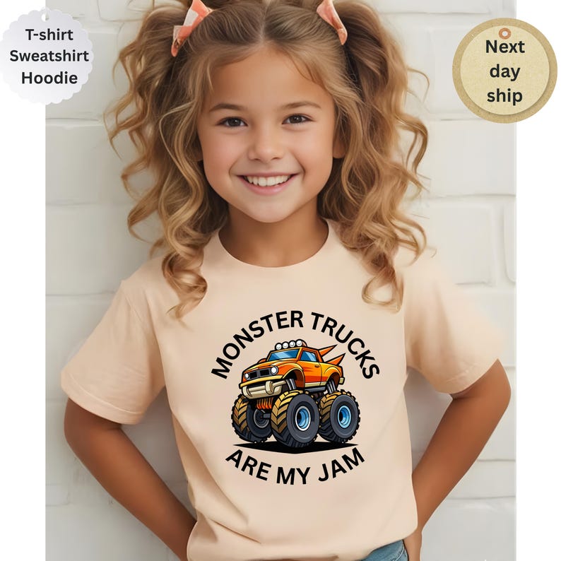 May include: A light peach-colored t-shirt featuring a colorful graphic of a monster truck with the text "MONSTER TRUCKS ARE MY JAM". The shirt is short-sleeved and has a round neckline. The image also includes text that says "T-shirt, Sweatshirt, Hoodie" and "Next day ship".