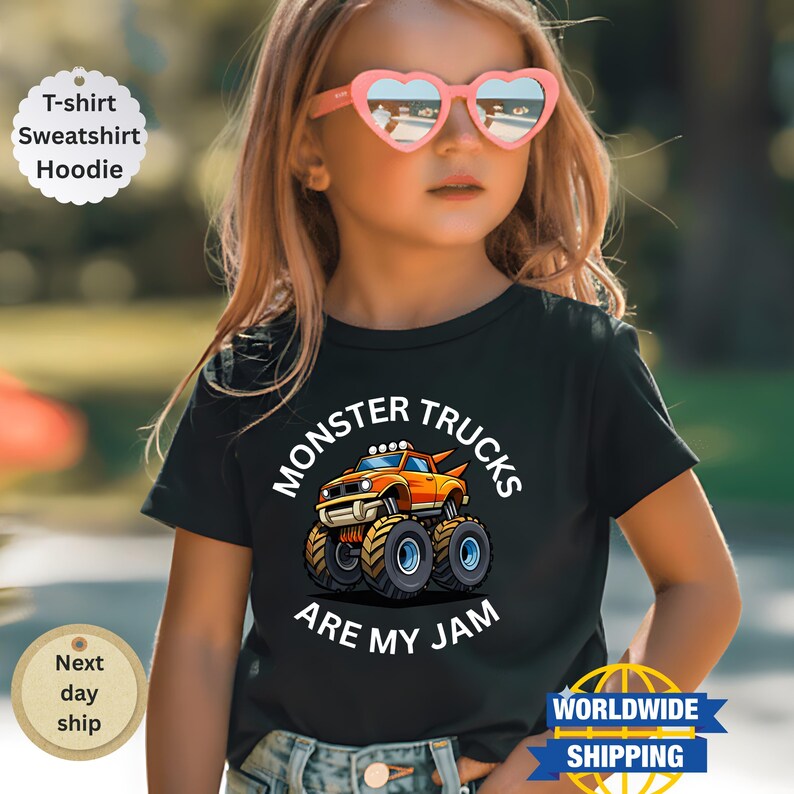 May include: A black t-shirt featuring a cartoon monster truck design in orange, yellow, and blue. The text "MONSTER TRUCKS ARE MY JAM" is printed above and below the truck graphic. The shirt is worn by a child.
