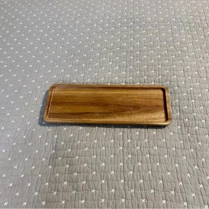 May include: A rectangular wooden tray with a warm brown finish. The tray has a slightly raised edge and is made of a solid wood material. The tray is empty and ready for use. Perfect for serving food or displaying items.