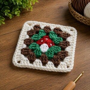 May include: A square crochet granny square featuring a central red and white mushroom motif surrounded by layers of dark brown and green yarn stitches, finished with an outer border of cream-colored yarn in a classic openwork pattern.