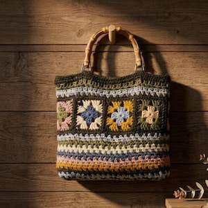 May include: A handmade crochet tote bag with a bamboo handle. The bag features a patchwork design with floral squares in shades of pink, blue, yellow, and green. The bag is hanging on a wooden wall, showcasing its rustic charm and craftsmanship.