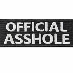 Può includere: Toppa rettangolare nera con testo ricamato bianco che recita "OFFICIAL ASSHOLE". La toppa ha un bordo nero ed è probabilmente progettata per essere cucita o stirata su vestiti o accessori.