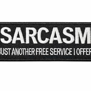 May include: Black rectangular patch with white embroidered text that reads "SARCASM" above "JUST ANOTHER FREE SERVICE I OFFER". The patch has a black border and is likely designed to be sewn or ironed onto clothing or accessories.