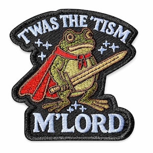 Peut inclure: Écusson brodé avec une grenouille de dessin animé portant une cape rouge et une épée. Le texte "T WAS THE 'TISM M'LORD" est en blanc sur fond noir. La grenouille est verte et beige, avec une écharpe rouge.