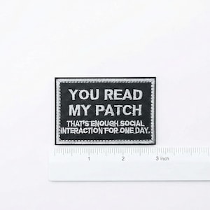 Puede incluir: Parche rectangular negro con texto bordado en blanco. El texto dice "YOU READ MY PATCH THAT'S ENOUGH SOCIAL INTERACTION FOR ONE DAY." El parche mide aproximadamente 7,6 cm de ancho y tiene un borde blanco.