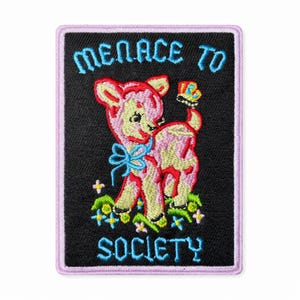 Può includere: Toppa ricamata con un design di agnello rosa, un fiocco blu e una farfalla. La toppa riporta le parole "MENACE TO SOCIETY" in blu su sfondo nero, incorniciate da un bordo lavanda. L'agnello è su un letto di fiori.