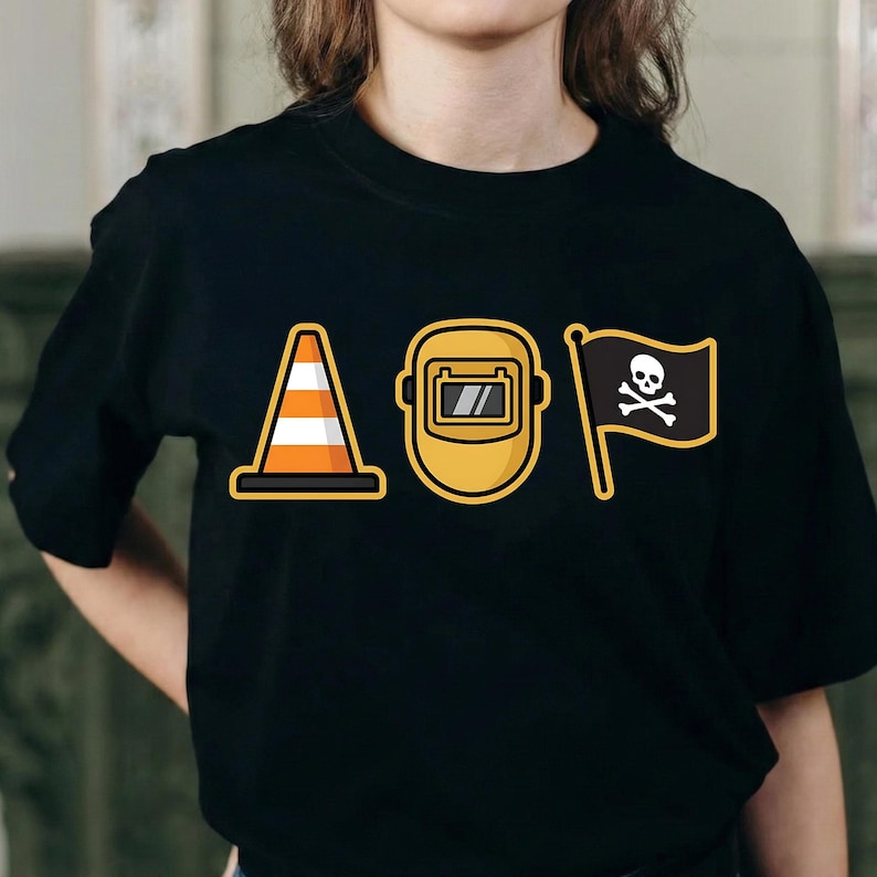 K&ouml;nnte beinhalten: Schwarzes T-Shirt mit drei Cartoon-Grafiken: einem orange-wei&szlig;en Verkehrskegel, einer gelben Schwei&szlig;maske und einer schwarzen Flagge mit Totenkopf und gekreuzten Knochen. Das Wort "AOP" ist impliziert.
