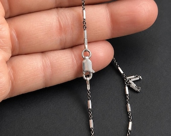 May include: A silver-toned chain necklace featuring a series of small, cylindrical metal beads spaced evenly along the links. The necklace includes a lobster claw clasp mechanism with a small rectangular tag stamped with the number 925.