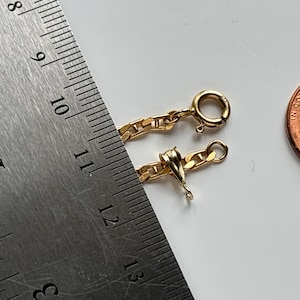 May include: A gold chain with a lobster clasp, next to a ruler showing measurements in inches. A penny is also in the image. The chain is approximately 11 inches long.