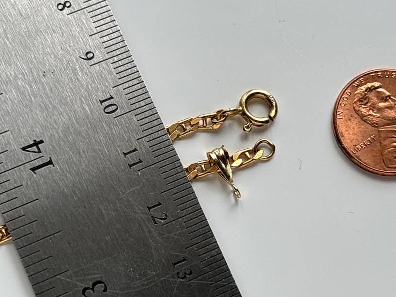 May include: A gold chain with a lobster clasp, next to a ruler showing measurements in inches. A penny is also in the image. The chain is approximately 11 inches long.
