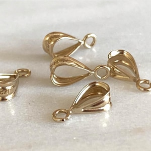 May include: A collection of gold-colored pendant bails. The bails have a teardrop shape with a small loop at the top and a wider opening at the bottom. One bail has the number "2019" engraved on it.