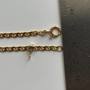 May include: A gold-colored chain necklace with a lobster clasp and a small pendant. The chain is measured with a ruler, showing a length of approximately 10 inches.