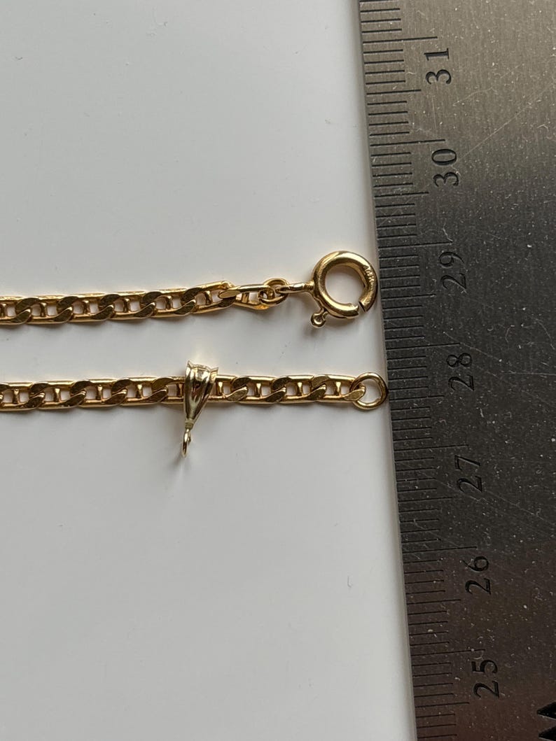 May include: A gold-colored chain necklace with a lobster clasp and a small pendant. The chain is measured with a ruler, showing a length of approximately 10 inches.