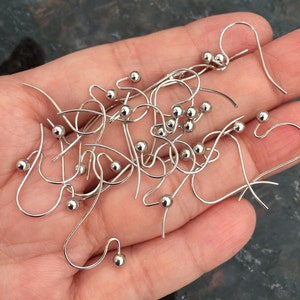 Puede incluir: Primer plano de un mont&oacute;n de ganchos para pendientes de plata con peque&ntilde;as bolas redondas en el extremo. Los ganchos son de metal y est&aacute;n dise&ntilde;ados para sujetar pendientes.