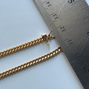 May include: A gold-colored curb chain necklace with a lobster clasp. The necklace is measured with a metal ruler, showing a length of approximately 12.5 inches. The chain links are closely linked together.