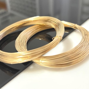 May include: Two circular coils of thin, metallic gold-colored wire. Each coil is formed by multiple continuous loops of wire, secured at one point with a small piece of the same gold-colored wire to maintain the circular shape and structure.