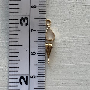 May include: A gold-colored jewelry bail with a teardrop-shaped setting. The bail measures approximately 0.75 inches in length. The bail is designed to hold a pendant or charm. The background is a light-colored wooden surface.