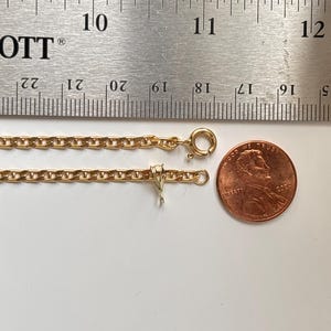 May include: A gold-colored chain necklace with a lobster clasp and a penny for size comparison. The necklace is next to a ruler showing measurements in inches.