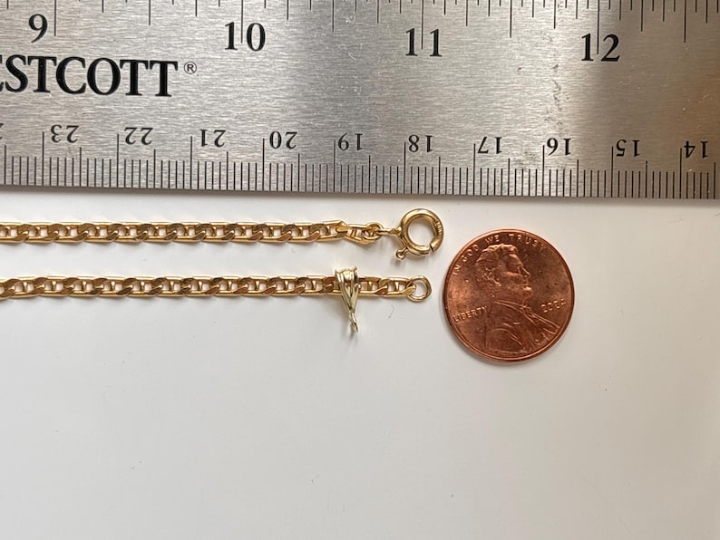 May include: A gold-colored chain necklace with a lobster clasp and a penny for size comparison. The necklace is next to a ruler showing measurements in inches.