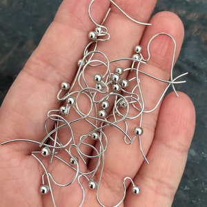 Puede incluir: Primer plano de un mont&oacute;n de ganchos de pendientes de plata con peque&ntilde;as bolas de plata en el extremo de cada gancho.