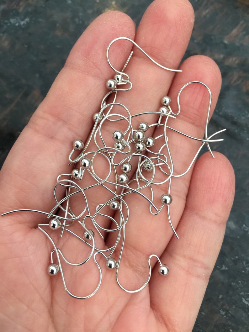 Puede incluir: Primer plano de un mont&oacute;n de ganchos de pendientes de plata con peque&ntilde;as bolas de plata en el extremo de cada gancho.