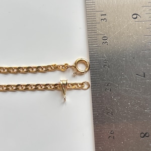May include: A gold-colored chain necklace with a lobster clasp and pendant bail. The chain is laid out next to a ruler, showing its length. The necklace is on a white surface.