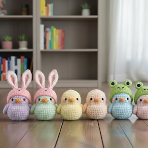 May include: Six crocheted amigurumi animals in a row. Two are bunnies with pink hats and ears, two are chicks, and two are frogs. The toys are in pastel colours and sit on a wooden surface.