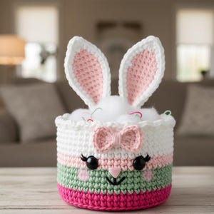 May include: A handmade crochet Easter basket shaped like a bunny. The basket is white, pink, green, and fuchsia, with a pink bow and black eyes. The bunny ears are white with pink insides. The basket is filled with white fluff.