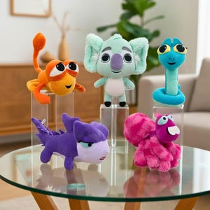May include: A collection of colorful plush toys, including an orange creature, a mint green koala, a blue snake, a purple dragon, and a pink creature. Each toy has large eyes and a friendly expression, displayed on clear pedestals.