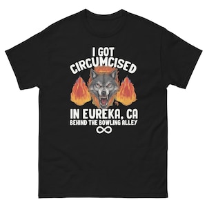 May include: Black t-shirt featuring a wolf's head graphic with flames and the text: "I GOT CIRCUMCISED IN EUREKA, CA BEHIND THE BOWLING ALLEY". An infinity symbol is below the text.