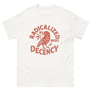 Puede incluir: Camiseta blanca con un gráfico rojo. El gráfico presenta un pájaro sosteniendo una ramita, rodeado por las palabras "RADICALIZED BY BASIC DECENCY" en un diseño circular. La camiseta tiene mangas cortas y cuello redondo.