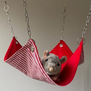 May include: A red and white striped fabric hammock with a plush grey chinchilla toy inside. The hammock is suspended by silver chains and rings, creating a cosy pet accessory.