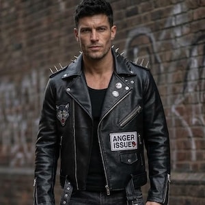 May include: Black leather jacket with silver spikes on the shoulders, a wolf patch, and a patch that reads "ANGER ISSUES." The jacket has a zipper closure and multiple pockets. The person is wearing black jeans.