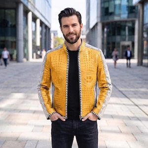 Könnte beinhalten: Eine gelbe Jacke mit einer strukturierten Krokodilleder-Optik auf den Vorder- und Rückenteilen, ergänzt durch graue Ärmel in Schlangenleder-Optik. Die Jacke verfügt über einen schwarz-weißen Zickzack-Besatz entlang des Reißverschlusses und der Ärmelbündchen.