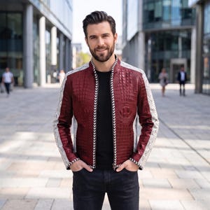 May include: A maroon jacket with a textured crocodile-skin pattern on the front and back panels, complemented by light grey snakeskin-patterned sleeves. The jacket features a black zip with a white and black chevron-patterned trim along the edges.