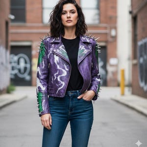 Può includere: Una giacca di pelle viola con borchie argentate sulle spalle e sul colletto. La giacca presenta un disegno dipinto di bianco e verde. La persona indossa una maglietta nera e jeans blu.