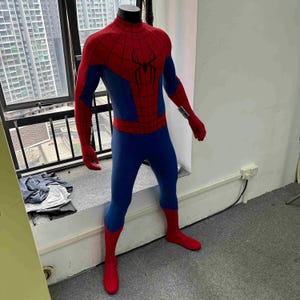 Pu&ograve; includere: Un costume completo di Spider-Man su un manichino. Il costume &egrave; rosso e blu, con un'emblema di ragno sul petto. Le sezioni rosse includono la testa, le braccia e i piedi. Le sezioni blu coprono il busto e le gambe.