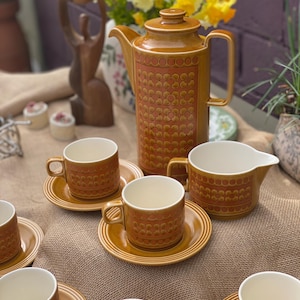 May include: A vintage brown ceramic tea set with a patterned design. The set includes a teapot, cups, saucers, and a creamer. The cups and teapot have a repeating pattern of small circles. The set is displayed on a burlap surface.