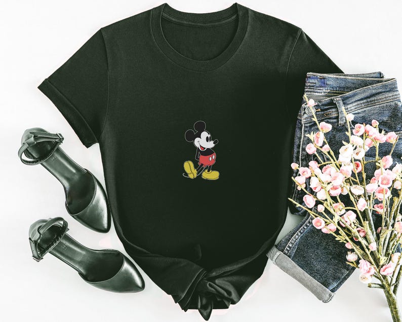Puede incluir: Camiseta negra con un peque&ntilde;o dise&ntilde;o bordado de Mickey Mouse. La camiseta se combina con pantalones cortos de mezclilla, tacones negros y un ramo de flores rosas. La camiseta tiene un cuello redondo cl&aacute;sico y mangas cortas.