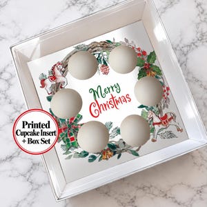 May include: A square white cupcake box with a clear lid and a printed insert featuring a Christmas wreath, two rocking horses, and the text Merry Christmas in red and green. The insert has six circular cutouts for holding cupcakes.
