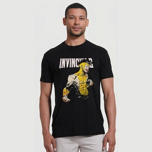 May include: Black t-shirt with the word "INVINCIBLE" in white above a yellow and white superhero graphic. The superhero is depicted in a fighting pose, showcasing muscles and a focused expression.
