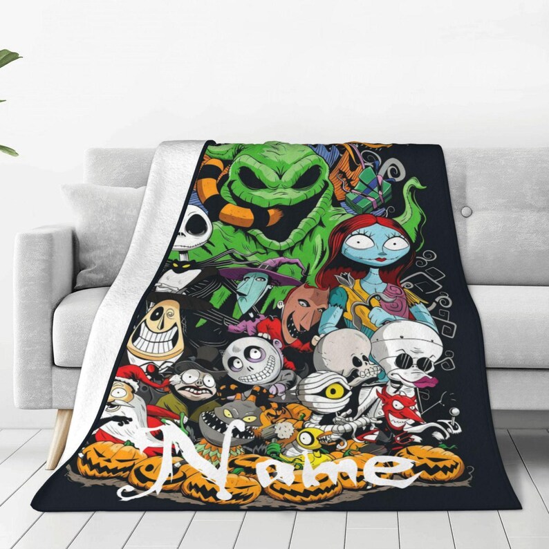Op de afbeelding: Een zwarte fleece deken met personages uit The Nightmare Before Christmas. De deken heeft een witte achterkant en een kleurrijk ontwerp van Jack Skellington, Sally en andere personages. Het woord "Name" is in het wit geschreven.