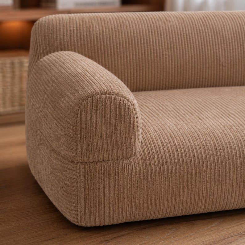 K&ouml;nnte beinhalten: Nahaufnahme eines beigefarbenen Cord-Sofas mit abgerundeter Armlehne. Das Sofa hat eine gerippte Textur und eine neutrale Farbe, passend f&uuml;r verschiedene Einrichtungsstile. Die Armlehne ist geschwungen und gut definiert.