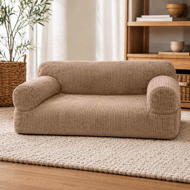 K&ouml;nnte beinhalten: Ein niedriges Sofa aus Cordstoff in einem neutralen Beigeton. Das Sofa hat abgerundete Armlehnen und eine rechteckige Basis, die f&uuml;r einen gem&uuml;tlichen Sitzbereich konzipiert ist. Es steht auf einem hellfarbigen Teppich, was auf eine Wohnzimmereinrichtung hindeutet.
