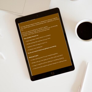 K&ouml;nnte beinhalten: Ein digitales Tablet zeigt den Text "The Calm Backend Reset Checklist" mit Aufz&auml;hlungszeichen auf einer wei&szlig;en Oberfl&auml;che. Ein Laptop, eine Kaffeetasse, ein Stift und ein dekorativer Gegenstand sind ebenfalls vorhanden.