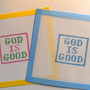 May include: Two square needlepoint canvases with white mesh fabric and colored tape borders. One canvas has a yellow border and features the text GOD IS GOOD in green and pink. The other has a light blue border with the text GOD IS GOOD in blue.