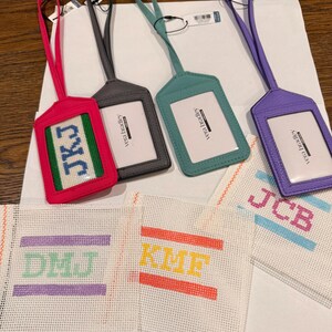 May include: A collection of personalized luggage tags in various colors, including pink, gray, teal, and purple. Each tag features a clear window for an ID and a matching strap. Also shown are needlepoint canvases with initials.